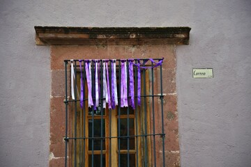Naklejka premium Colonial house window with stone trim, handcrafted iron grilles and colorful satin ribbons in San Miguel de Allende, Guanajuato Mexico.