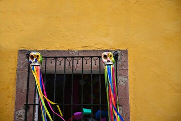 Naklejka premium Colonial Art shop window with a stone trim, colorful hand painted clay masks and satin ribbons on an ochre stucco wall in San Miguel de Allende, Mexico.