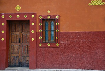 Naklejka premium Colonial house facade with an antique wooden door and window on a Venetian red stucco wall in San Miguel de Allende, Guanajuato Mexico.