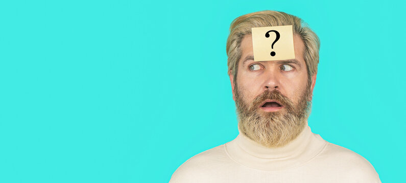 Surprised bearded man with question mark on blue background. Man with question mark on forehead looking up. Paper notes with question marks. Copy spase