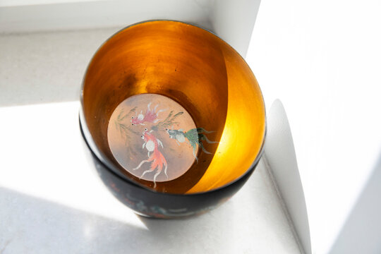 Interior view of black lacquer bowl with golden surface and painted goldfish swimming among aquatic plants at the base