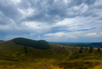 Fototapeta premium serene hills and clouds over a grassy hilltop landscape with a tranquil sky and vibrant green and blue hues in an outdoor setting, viewed from a hilltop looking out over the scenic view.