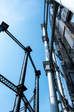 Exposed pipes and steel structures rising beside a modern building under blue sky with a crane creating a vertical engineering architecture composition