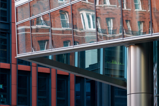 Reflective glass facade mirroring red brick architecture across windows and steel structure in a layered contrast between modern and traditional buildings