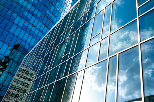 Glass facade with reflective windows and geometric lines against a blue sky creating an abstract pattern across contemporary urban architecture