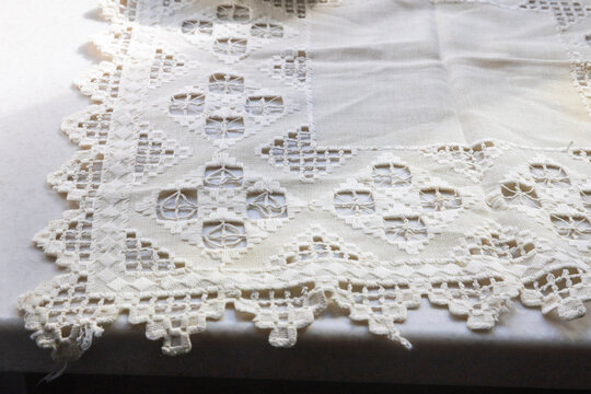 White Hardanger embroidery tablecloth featuring geometric cutwork patterns and a scalloped lace edge spread across a flat surface.