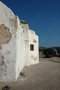 The traditional weathered white apsidal wall of the historic Church of Panagia Myrtidiotissa features a small window inside Chora fortress on Kythira island