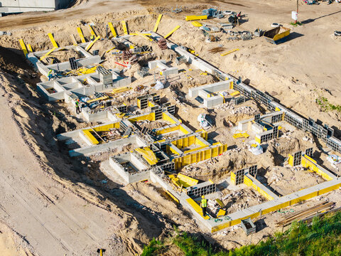 Aerial view of a construction site featuring concrete foundations, yellow formwork, and workers in safety vests in Riga, Latvia.