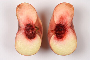 A top view of a fresh flat saturn peach cut into two halves showing the inner pit and flesh on a plain white surface. © nahhan