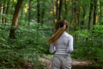 Fototapeta premium Woman jogging through green forest. Horizontal outdoor running scene.
