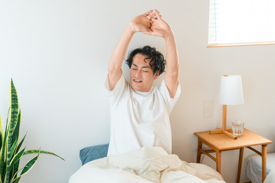 A middle-aged Asian man wakes up in the morning and stretches comfortably in bed.