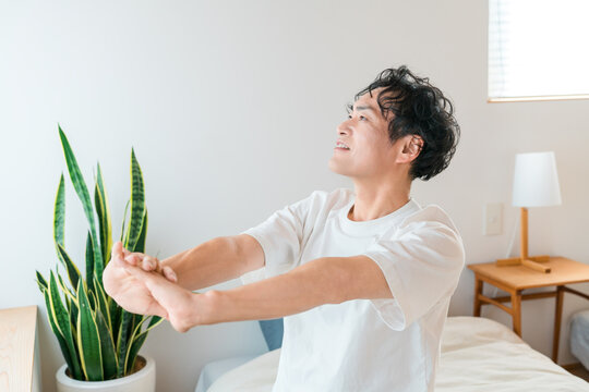 A middle-aged Asian man wakes up in the morning and stretches comfortably in bed.