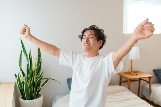 A middle-aged Asian man wakes up in the morning and stretches comfortably in bed.
