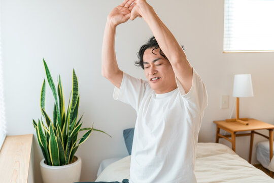 A middle-aged Asian man wakes up in the morning and stretches comfortably in bed.