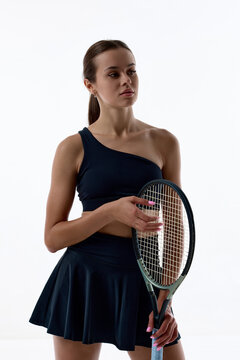 Confident female tennis player posing with racket on white studio background. Concept of athlete portrait, sports confidence, professional image.