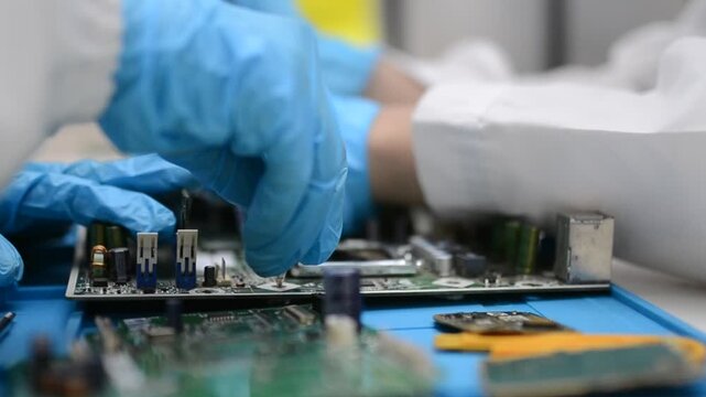 Gloved technician hand soldering components on printed circuit board in factory