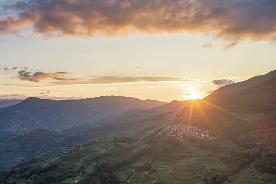 Aerial view of terraced rice fields in Yuanyang County at sunset with rolling mountains and a village, Honghe Hani and Yi Autonomous Prefecture, Yunnan, China.