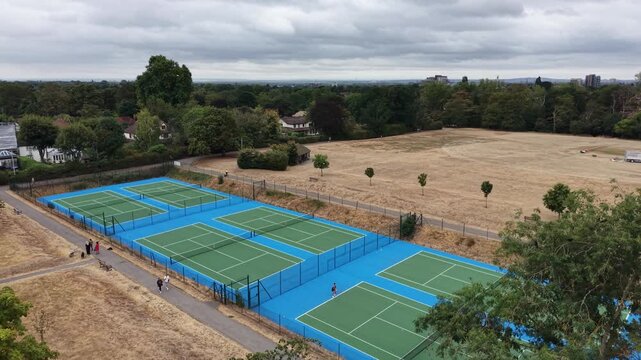 4K UHD drone diagonal tracking shot panning and approaching six newly renovated tennis courts at beautiful Raphael Park, Romford, England. Modern sports facility reveal