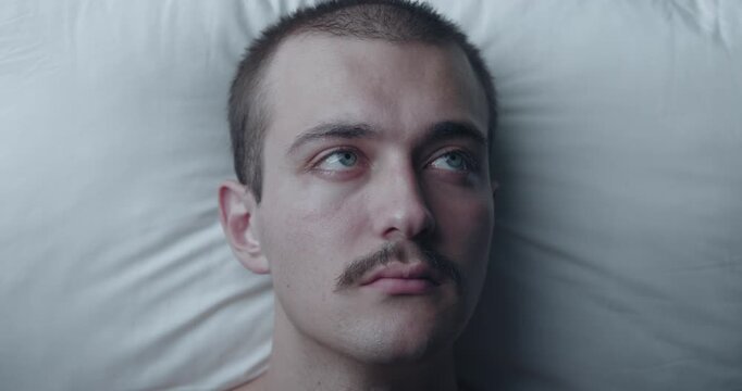 Top Down Portrait of Thoughtful Young Caucasian Man Lying Awake in Bed with Insomnia