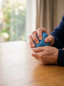 Elderly person squeezing blue stress ball for physical therapy rehabilitation