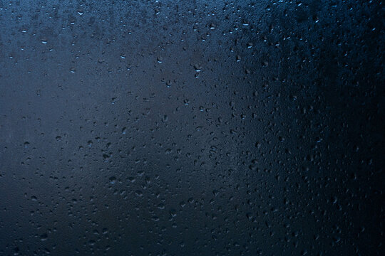 Abstract blue background with condensation and water droplets on glass. Dark atmospheric texture with blurred light and copy space.