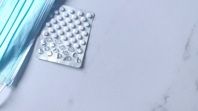Woman's hand picks up a blister pack of pills from a table with another blister pack and a medical face mask, healthcare concept.