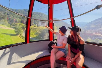 mother and daughter in cable car gondola over Alpine valley and pine forest, Seceda, Val Gardena, Dolomites, Italy  © Angelov