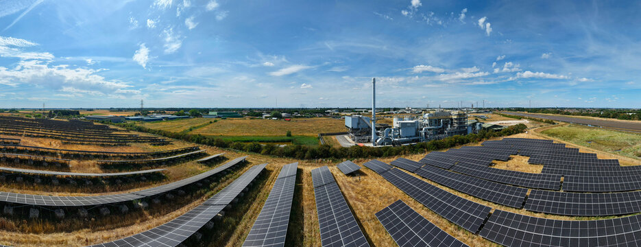 Aerial view of a biomass energy power plant surrounded by extensive solar farms in a rural landscape under a clear blue sky in Boston, England, United Kingdom.