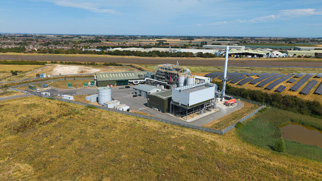 Aerial view of a biomass energy power plant with adjacent solar farms, industrial buildings, and storage tanks in a rural landscape under a clear blue sky in Boston, England, United Kingdom.