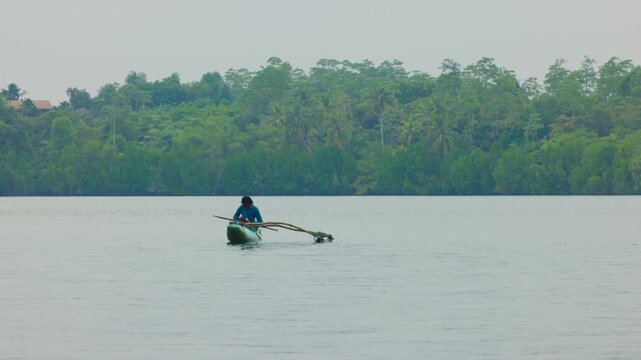 A local fisherman in a traditional Sri Lankan outrigger dugout boat (oruwa) navigates the calm waters of a body of water in Sri Lanka. fisherman swims in slow motion video. 10.02.2022 SRI LANKA.
