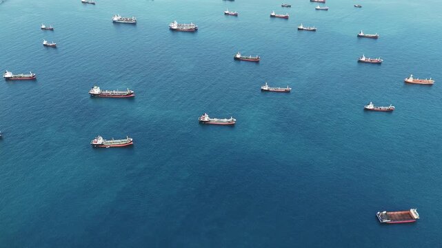 Fleet of oil tanker ships and commercial cargo vessels anchored in the deep blue sea near a long bridge. Global maritime logistics, international shipping trade, and energy transport.