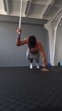 Muscular man performs a dynamic rope-assisted push-up, lifting his body from the floor. Upper body strength, grip, power and functional fitness concepts. Vertical video.