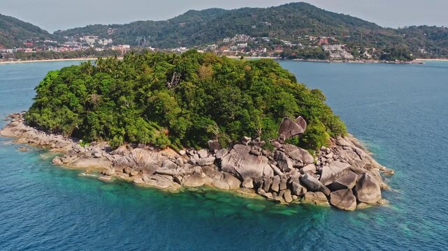 Phuket island, Ko Pu small uninhabited island covered in lush green jungle and large rock formations, rises from clear turquoise waters of Andaman Sea near Kata Beach, Thailand. Aerial drone flight