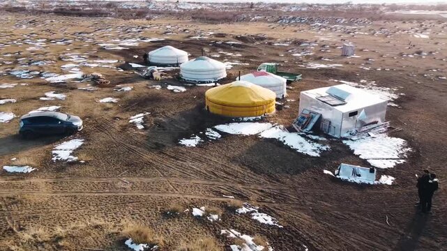 Aerial view of colorful traditional yurts and gers scattered across a vast steppe landscape with patches of melting snow in Mini Gobi, Mongolia