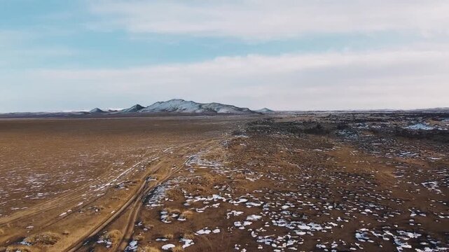 Aerial view descending over a dirt road cutting through sparse arid terrain with scattered snow patches and distant mountains in Mini Gobi, Mongolia