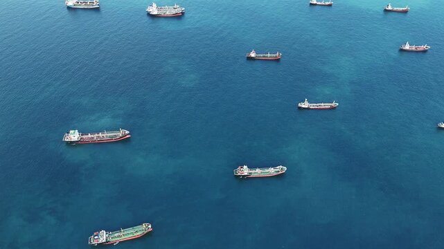 Fleet of oil tanker ships and commercial cargo vessels anchored in the deep blue sea near a long bridge. Global maritime logistics, international shipping trade, and energy transport.