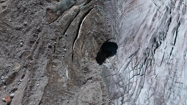 Aerial view of deep glacial crevasse and melting ice cave in high mountain terrain.
