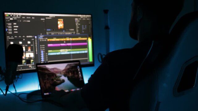 Video editor at workstation monitors timeline playback with sound level meters and laptop preview in a dark creative studio, ideal for post production, editing, and media workflow.