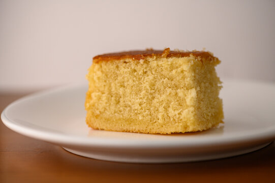 Golden cake slice rests on a white plate, invitingly showcasing its soft texture and warm color under soft lighting