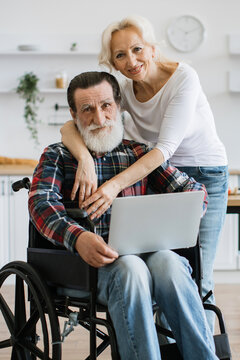 A smiling woman embraces a man in a wheelchair as they look at a laptop together in a bright, modern kitchen