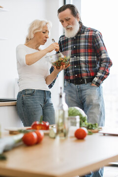 An elderly couple happily prepares a fresh salad together in a bright, modern kitchen, showcasing a healthy lifestyle