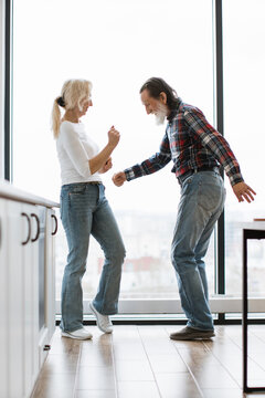 An elderly couple shares a moment of fun and connection, dancing together in their home with a large window providing natural light