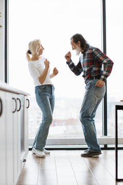 An energetic elderly couple enjoys a joyful moment dancing together indoors with a large window providing natural light
