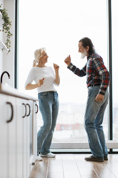 An energetic elderly couple joyfully dances in their bright, modern kitchen, celebrating life and togetherness