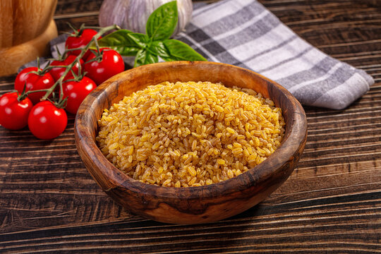 Bulgur wheat in wooden bowl with cherry tomatoes basil and garlic on rustic table