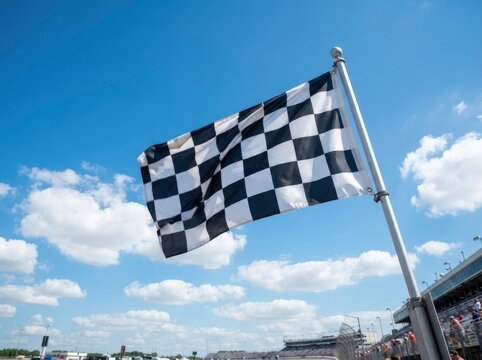 A checkered flag waving on a pole against a bright blue sky with clouds, representing a finish line or victory at a sporting event or race track.