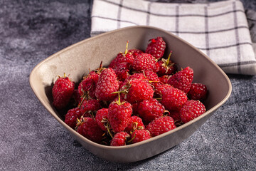 Fresh raspberries in ceramic bowl on textured surface with checkered cloth © Andrei Starostin