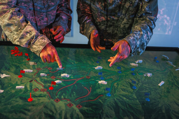 Naklejka premium Military personnel in camouflage uniforms point at a digital terrain map during a tactical planning briefing.