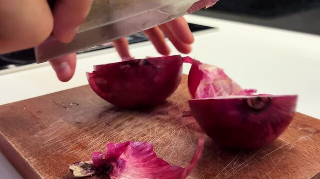 Close-up of a person slicing a fresh onion with a kitchen knife on a cutting board. Simple food preparation process suitable for cooking, healthy eating and homemade meal concepts.