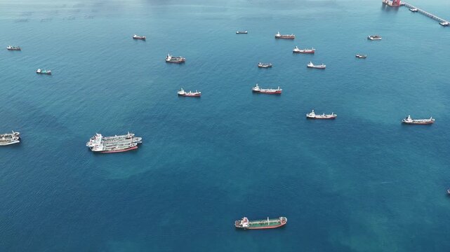 Fleet of oil tanker ships and commercial cargo vessels anchored in the deep blue sea near a long bridge. Global maritime logistics, international shipping trade, and energy transport.